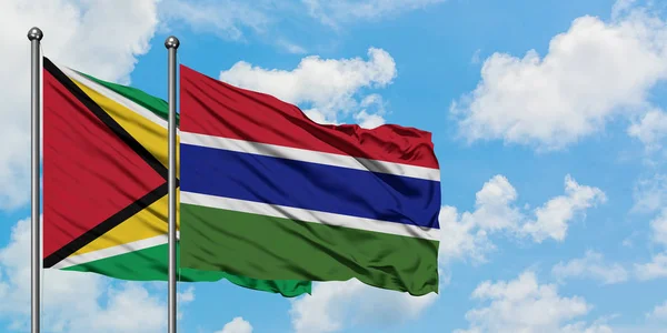 Bandera de Guyana y Gambia ondeando en el viento contra el cielo azul nublado blanco juntos. Concepto diplomático, relaciones internacionales . — Foto de Stock