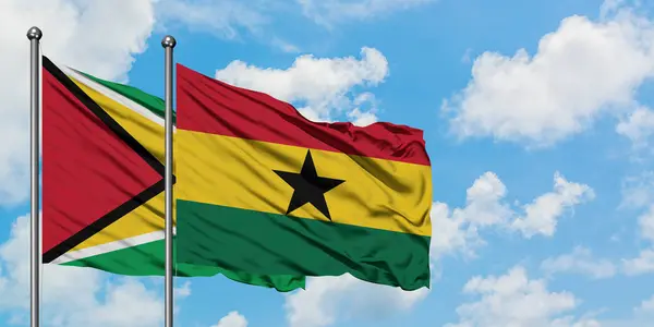 Gujana i Ghana flagi machając w wiatr przed białym zachmurzone błękitne niebo razem. Koncepcja dyplomacji, stosunki międzynarodowe. — Zdjęcie stockowe