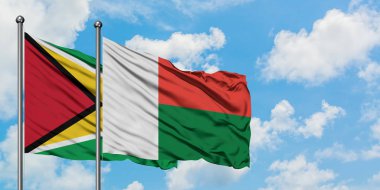 Guyana ve Madagaskar bayrağı birlikte beyaz bulutlu mavi gökyüzüne karşı rüzgarda sallayarak. Diplomasi kavramı, uluslararası ilişkiler.