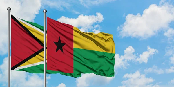 Guyana e Guinea Bissau sventolano nel vento contro il bianco cielo blu nuvoloso insieme. Concetto di diplomazia, relazioni internazionali . — Foto Stock