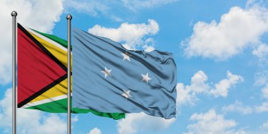 Guyana ve Mikronezya bayrağı birlikte beyaz bulutlu mavi gökyüzüne karşı rüzgarda sallayarak. Diplomasi kavramı, uluslararası ilişkiler.