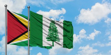 Guyana ve Norfolk Adası bayrağı birlikte beyaz bulutlu mavi gökyüzüne karşı rüzgarda sallayarak. Diplomasi kavramı, uluslararası ilişkiler.