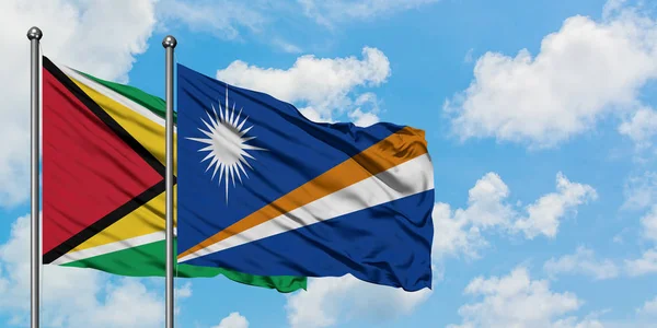 Die Flaggen von Guyana und den Marshallinseln wehen gemeinsam im Wind vor dem wolkenverhangenen blauen Himmel. Diplomatie-Konzept, internationale Beziehungen. — Stockfoto