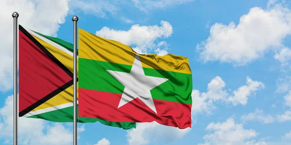 Bandera de Guyana y Myanmar ondeando en el viento contra el cielo azul nublado blanco juntos. Concepto diplomático, relaciones internacionales . — Foto de Stock