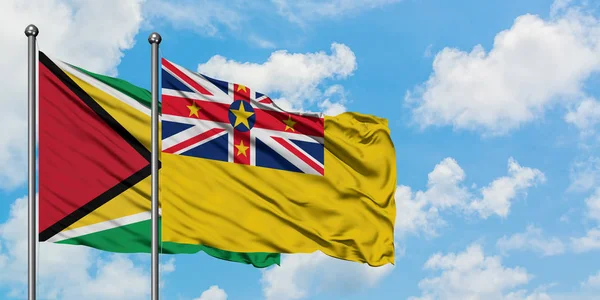 Bandera de Guyana y Niue ondeando en el viento contra el cielo azul nublado blanco juntos. Concepto diplomático, relaciones internacionales . — Foto de Stock