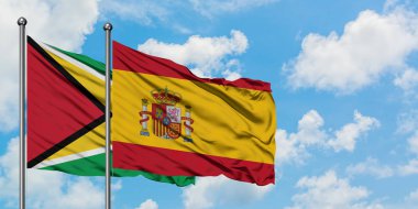 Guyana ve İspanya bayrağı birlikte beyaz bulutlu mavi gökyüzüne karşı rüzgarda sallayarak. Diplomasi kavramı, uluslararası ilişkiler.