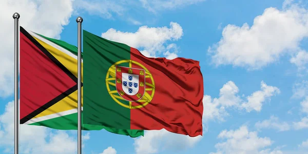 Guiana e bandeira de Portugal agitando no vento contra o céu azul nublado branco juntos. Conceito de diplomacia, relações internacionais . — Fotografia de Stock