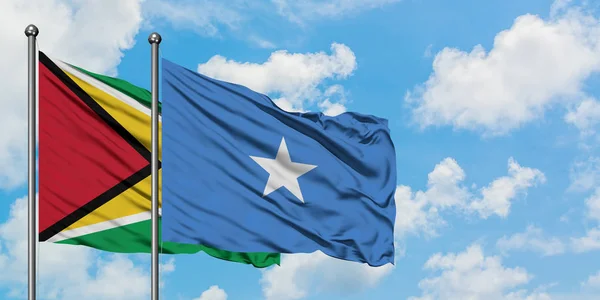 Bandera de Guyana y Somalia ondeando en el viento contra el cielo azul nublado blanco juntos. Concepto diplomático, relaciones internacionales . — Foto de Stock