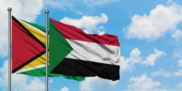 Bandera de Guyana y Sudán ondeando en el viento contra el cielo azul nublado blanco juntos. Concepto diplomático, relaciones internacionales . — Foto de Stock