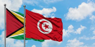 Guyana ve Tunus bayrağı birlikte beyaz bulutlu mavi gökyüzüne karşı rüzgarda sallayarak. Diplomasi kavramı, uluslararası ilişkiler.