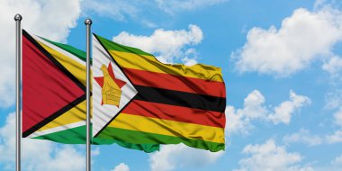 Guyana ve Zimbabve bayrağı birlikte beyaz bulutlu mavi gökyüzüne karşı rüzgarda sallayarak. Diplomasi kavramı, uluslararası ilişkiler.