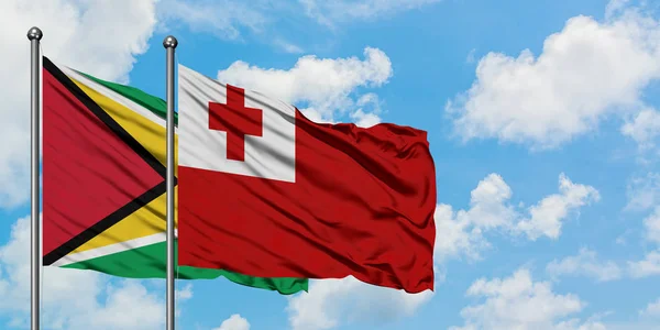 Bandera de Guyana y Tonga ondeando en el viento contra el cielo azul nublado blanco juntos. Concepto diplomático, relaciones internacionales . — Foto de Stock