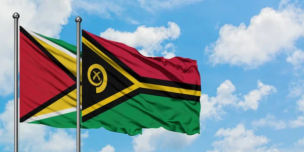 Gujana i Vanuatu flagi machając w wiatr przed białym zachmurzone błękitne niebo razem. Koncepcja dyplomacji, stosunki międzynarodowe. — Zdjęcie stockowe