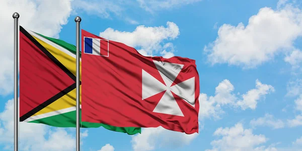 Guyana y Wallis y la bandera de Futuna ondeando en el viento contra el cielo azul nublado blanco juntos. Concepto diplomático, relaciones internacionales . — Foto de Stock