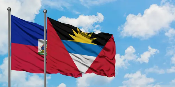 Haití y Antigua y Barbuda ondeando en el viento contra el cielo azul nublado blanco juntos. Concepto diplomático, relaciones internacionales . —  Fotos de Stock