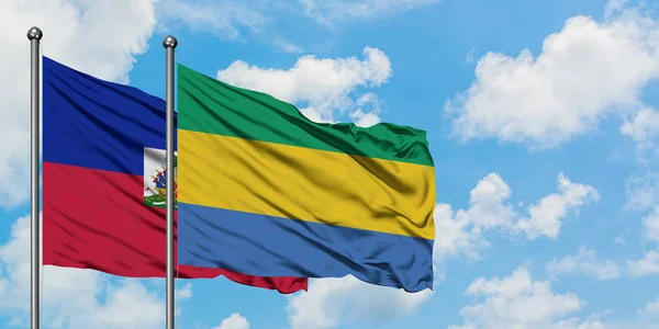 Bandera de Haití y Gabón ondeando en el viento contra el cielo azul nublado blanco juntos. Concepto diplomático, relaciones internacionales . — Foto de Stock