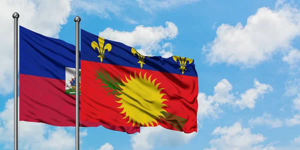 Bandera de Haití y Guadalupe ondeando en el viento contra el cielo azul nublado blanco juntos. Concepto diplomático, relaciones internacionales . — Foto de Stock