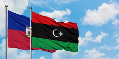 Haiti ve Libya bayrağı birlikte beyaz bulutlu mavi gökyüzüne karşı rüzgarda sallayarak. Diplomasi kavramı, uluslararası ilişkiler.