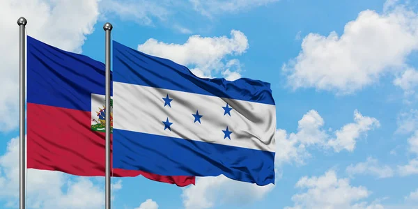 Bandeira do Haiti e Honduras agitando no vento contra o céu azul nublado branco juntos. Conceito de diplomacia, relações internacionais . — Fotografia de Stock