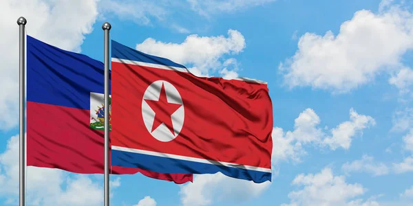 A bandeira do Haiti e da Coreia do Norte agitando no vento contra o céu azul nublado branco juntos. Conceito de diplomacia, relações internacionais . — Fotografia de Stock
