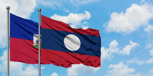 Bandera de Haití y Laos ondeando en el viento contra el cielo azul nublado blanco juntos. Concepto diplomático, relaciones internacionales . — Foto de Stock