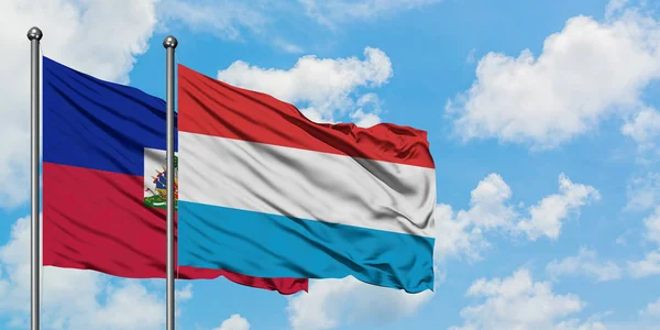 Haiti i Luksemburg flaga machając w wiatr przed białym zachmurzone błękitne niebo razem. Koncepcja dyplomacji, stosunki międzynarodowe. — Zdjęcie stockowe