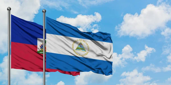 A bandeira do Haiti e da Nicarágua agitando no vento contra o céu azul nublado branco juntos. Conceito de diplomacia, relações internacionais . — Fotografia de Stock