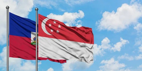 A bandeira do Haiti e de Singapura agitando no vento contra o céu azul nublado branco juntos. Conceito de diplomacia, relações internacionais . — Fotografia de Stock