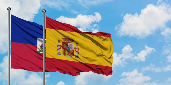 Bandera de Haití y España ondeando en el viento contra el cielo azul nublado blanco juntos. Concepto diplomático, relaciones internacionales . — Foto de Stock