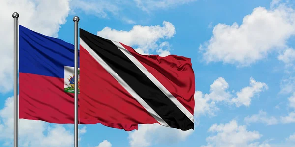 Bandera de Haití y Trinidad y Tobago ondeando en el viento contra el cielo azul nublado blanco juntos. Concepto diplomático, relaciones internacionales . —  Fotos de Stock