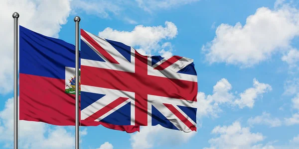 Bandera de Haití y Reino Unido ondeando en el viento contra el cielo azul nublado blanco juntos. Concepto diplomático, relaciones internacionales . — Foto de Stock