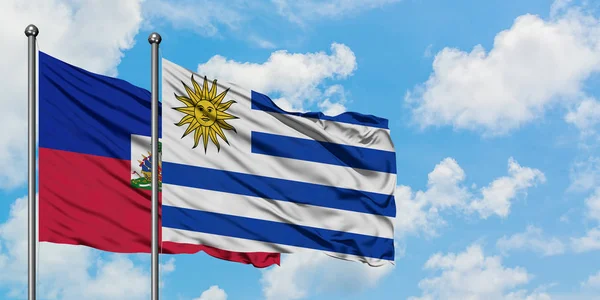 Bandera de Haití y Uruguay ondeando en el viento contra el cielo azul nublado blanco juntos. Concepto diplomático, relaciones internacionales . —  Fotos de Stock