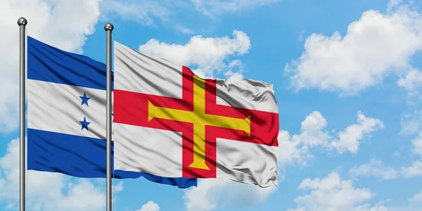 Bandera de Honduras y Guernsey ondeando en el viento contra el cielo azul nublado blanco juntos. Concepto diplomático, relaciones internacionales . — Foto de Stock