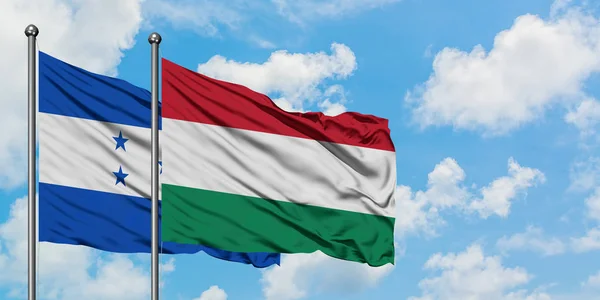 Bandera de Honduras y Hungría ondeando en el viento contra el cielo azul nublado blanco juntos. Concepto diplomático, relaciones internacionales . — Foto de Stock