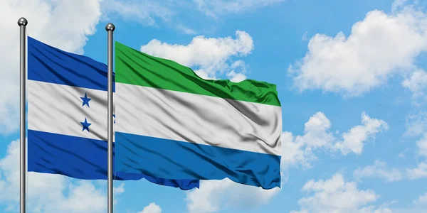 Bandera de Honduras y Sierra Leona ondeando en el viento contra el cielo azul nublado blanco juntos. Concepto diplomático, relaciones internacionales . — Foto de Stock