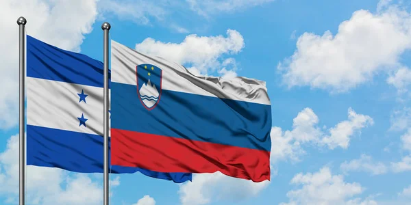 Honduras and Slovenia flag waving in the wind against white cloudy blue sky together. Diplomacy concept, international relations.