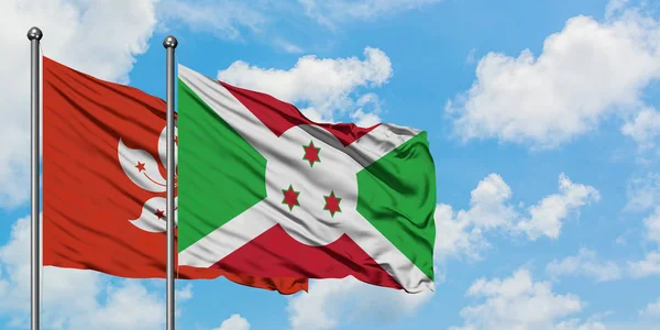 Bandera de Hong Kong y Burundi ondeando en el viento contra el cielo azul nublado blanco juntos. Concepto diplomático, relaciones internacionales . — Foto de Stock