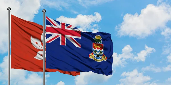 Bandera de Hong Kong y las Islas Caimán ondeando en el viento contra el cielo azul nublado blanco juntos. Concepto diplomático, relaciones internacionales . — Foto de Stock
