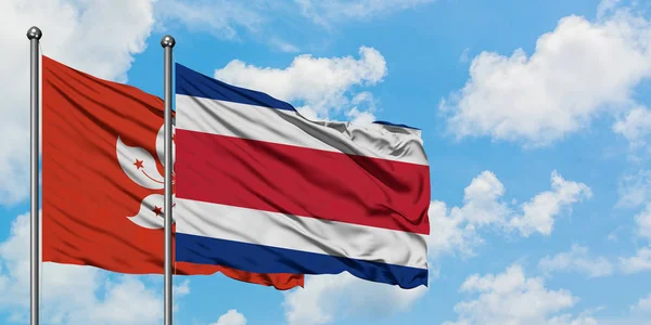 Bandeira de Hong Kong e Costa Rica agitando no vento contra o céu azul nublado branco juntos. Conceito de diplomacia, relações internacionais . — Fotografia de Stock