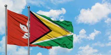 Hong Kong ve Guyana bayrağı birlikte beyaz bulutlu mavi gökyüzüne karşı rüzgarda sallayarak. Diplomasi kavramı, uluslararası ilişkiler.