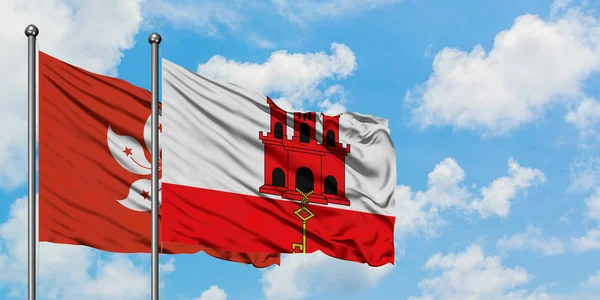 Drapeau de Hong Kong et Gibraltar agitant dans le vent contre ciel bleu nuageux blanc ensemble. Concept de diplomatie, relations internationales . — Photo