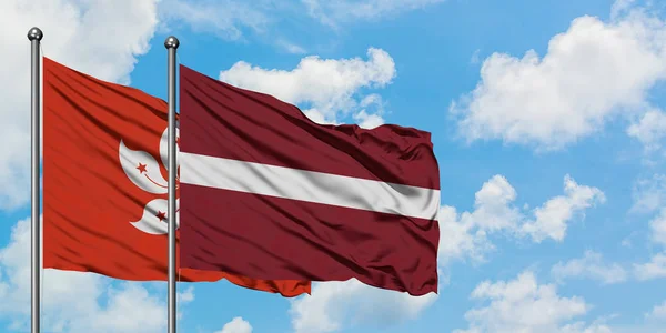 Bandeira de Hong Kong e Letônia agitando no vento contra o céu azul nublado branco juntos. Conceito de diplomacia, relações internacionais . — Fotografia de Stock