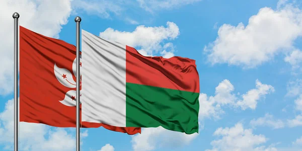 Bandera de Hong Kong y Madagascar ondeando en el viento contra el cielo azul nublado blanco juntos. Concepto diplomático, relaciones internacionales . — Foto de Stock