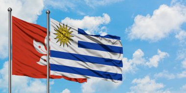 Hong Kong ve Uruguay bayrağı birlikte beyaz bulutlu mavi gökyüzüne karşı rüzgarda sallayarak. Diplomasi kavramı, uluslararası ilişkiler.