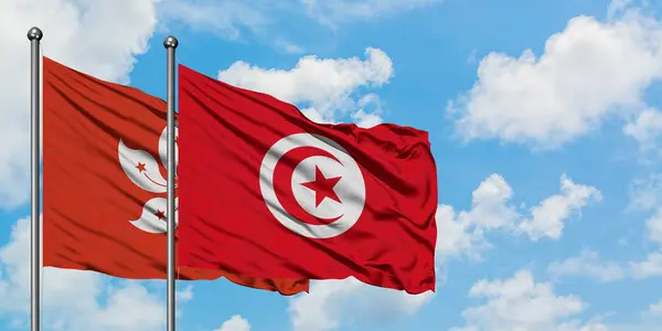 香港和突尼斯国旗在风中飘扬，与白云蓝天相一起。外交概念、国际关系. — 图库照片