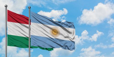 Macaristan ve Arjantin bayrağı birlikte beyaz bulutlu mavi gökyüzüne karşı rüzgarda sallayarak. Diplomasi kavramı, uluslararası ilişkiler.