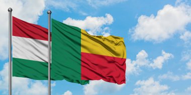 Macaristan ve Benin bayrağı birlikte beyaz bulutlu mavi gökyüzüne karşı rüzgarda sallayarak. Diplomasi kavramı, uluslararası ilişkiler.