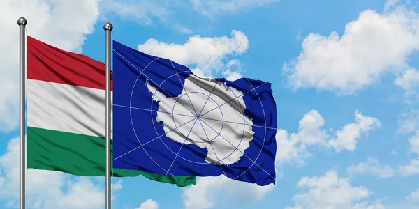 Bandera de Hungría y la Antártida ondeando en el viento contra el cielo azul nublado blanco juntos. Concepto diplomático, relaciones internacionales . — Foto de Stock