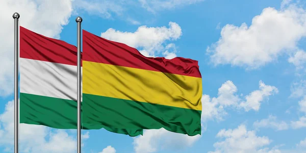 Bandera de Hungría y Bolivia ondeando en el viento contra el cielo azul nublado blanco juntos. Concepto diplomático, relaciones internacionales . — Foto de Stock