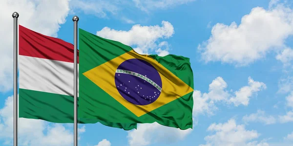 Bandera de Hungría y Brasil ondeando en el viento contra el cielo azul nublado blanco juntos. Concepto diplomático, relaciones internacionales . — Foto de Stock